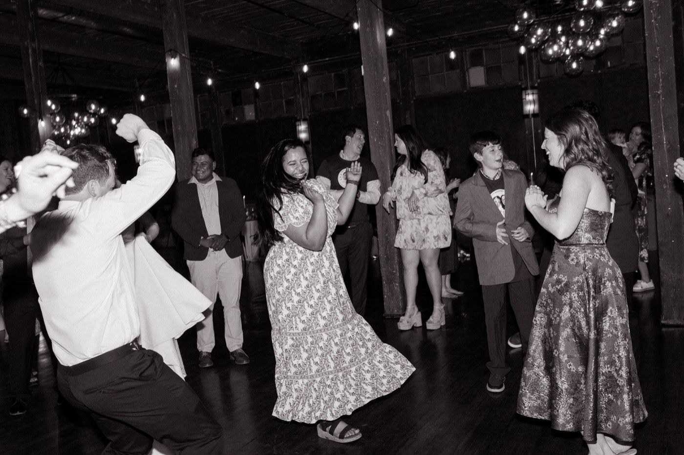 Black-and-white photo of guests dancing and laughing on a dark wooden dance floor