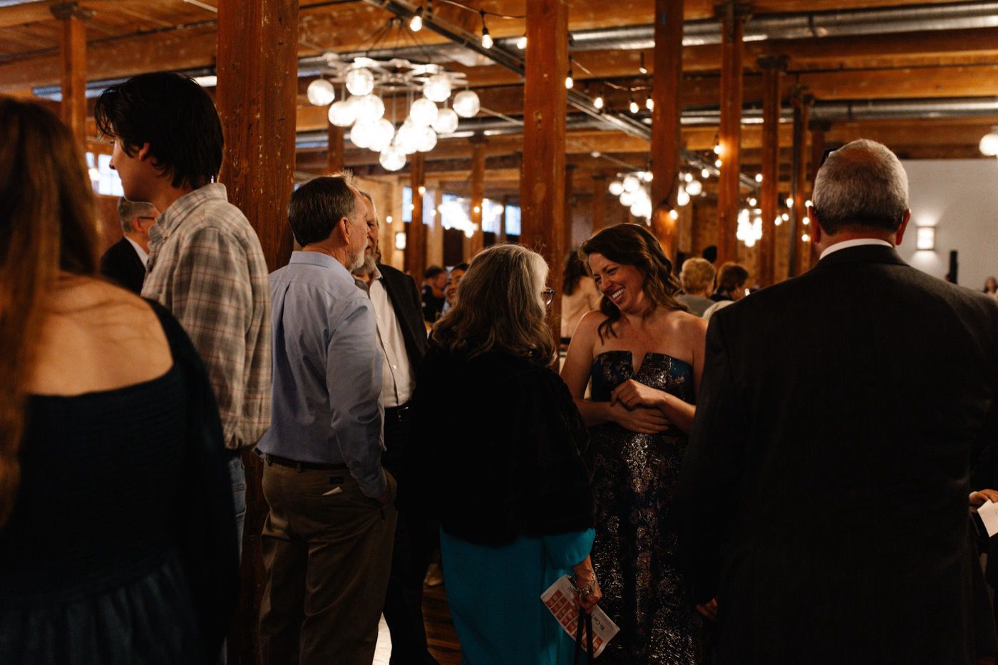 Guests chatting and laughing in a warm wood-beamed venue lit by globe lights