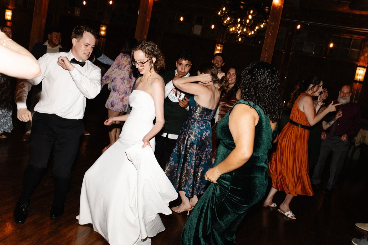 A bride and groom dancing with wedding guests on a wooden dance floor under string lights